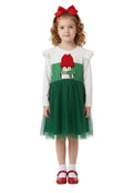 Young girl wearing a green and red dress with a white top, standing against a white background.