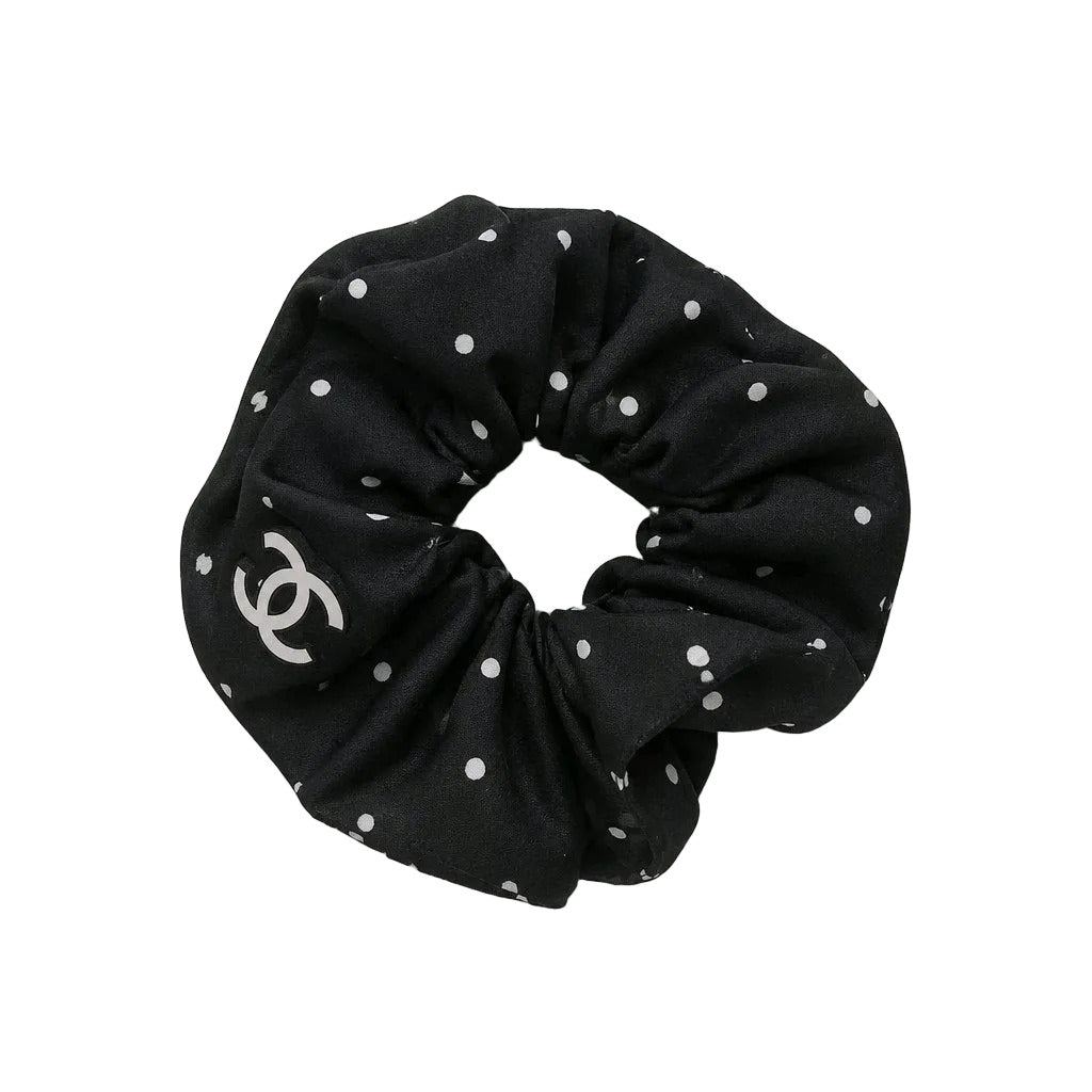 Black scrunchie with white polka dots and a logo on a light gray background