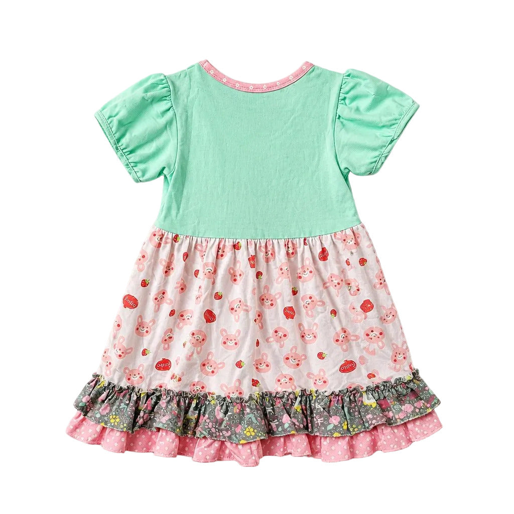 A baby girl's dress with a solid mint green bodice and a white skirt featuring a strawberry and bunny print, finished with a ruffled floral hem.