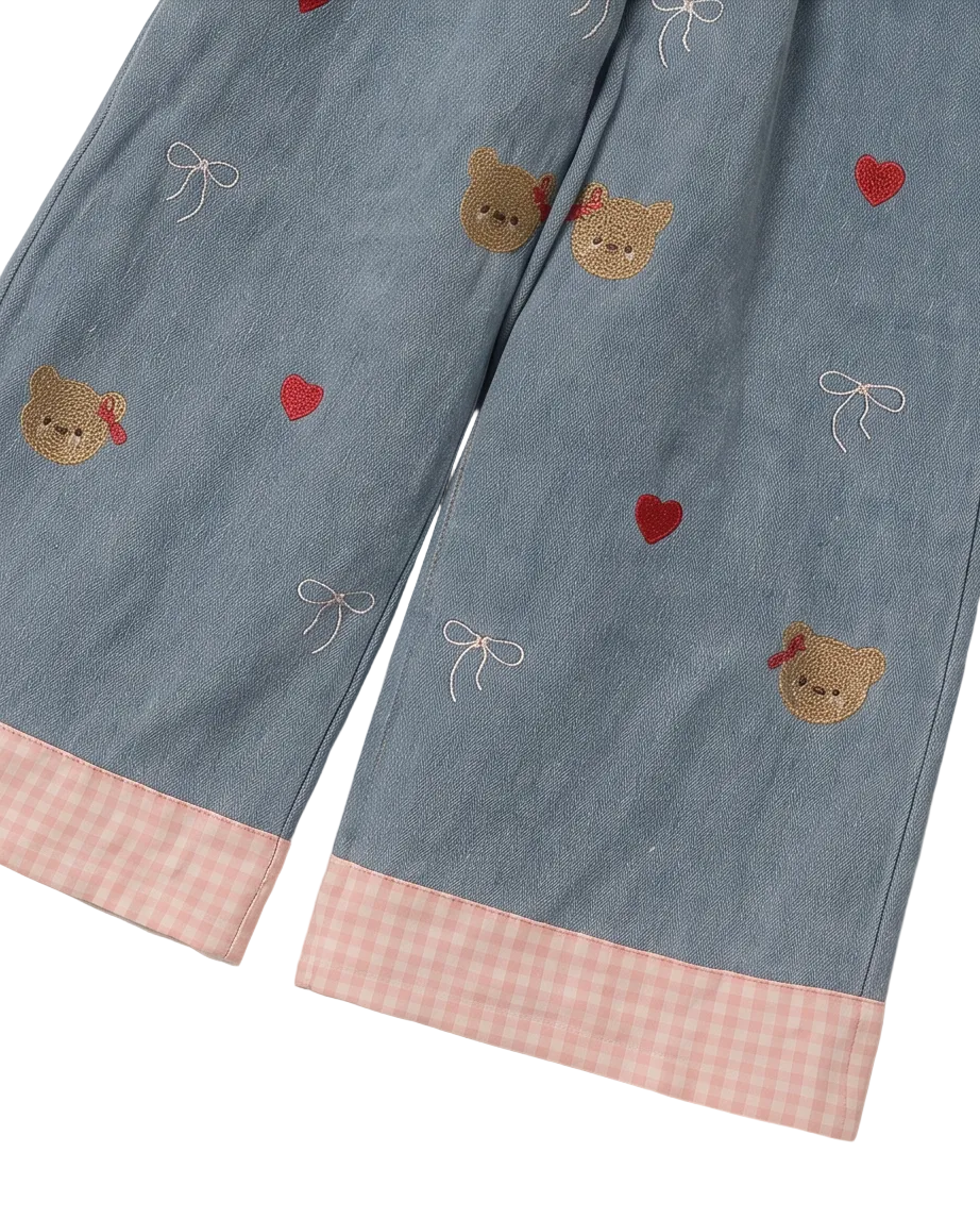 Light blue denim pajama pants with embroidered teddy bear faces, red hearts, white bows, and pink gingham cuffs, shown on a light gray background.