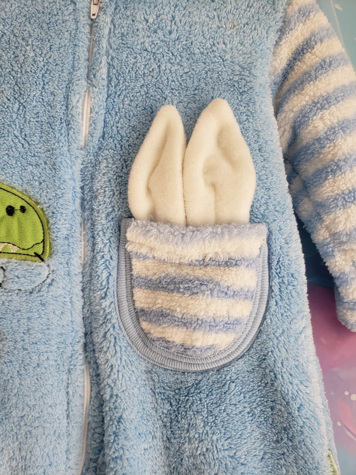 Close-up of a blue fleece jacket with a pocket featuring cream-colored bunny ears and striped sleeves.