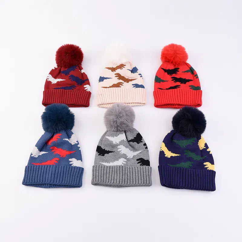 A collection of children's woolen hats with dinosaur prints and pom-pom toppings in various colors.